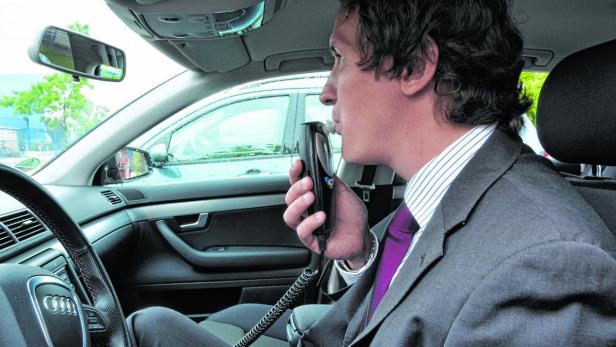 Ein Mann im Anzug führt in einem Auto einen Alkoholtest durch.
