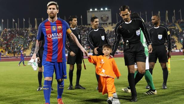 Lionel Messi betritt mit einem Kind an der Hand das Fußballfeld.