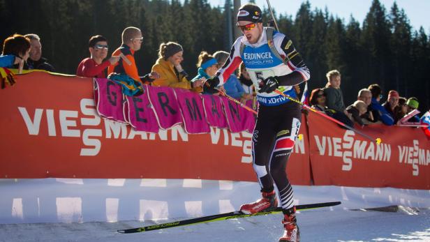 Ein Biathlet läuft auf Skiern an einer Zuschauertribüne vorbei.