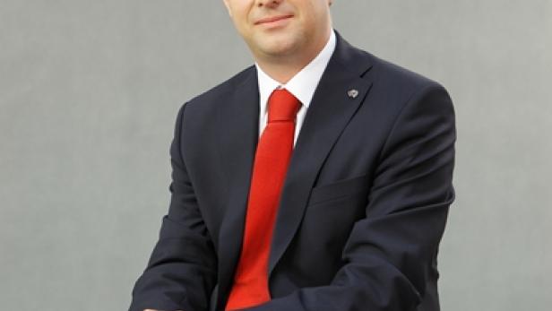 Ein Mann in Anzug und roter Krawatte sitzt auf einer weißen Oberfläche.