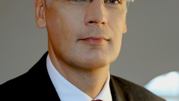 Ein Mann mit Brille, Anzug und roter Krawatte blickt in die Kamera.