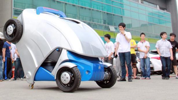 Ein futuristisch anmutendes, blau-silbernes Fahrzeug mit vier Rädern steht im Freien.