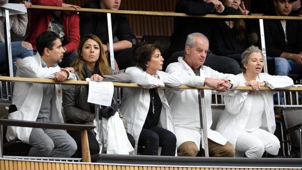 Eine Gruppe von Personen in weißen Kitteln lehnt an einer hölzernen Balustrade.