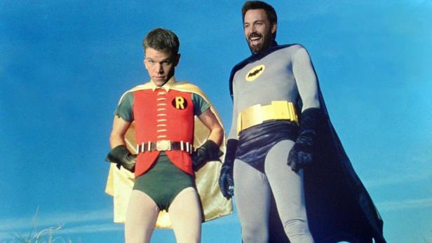 Matt Damon als Robin und Ben Affleck als Batman in Kostümen vor blauem Himmel.
