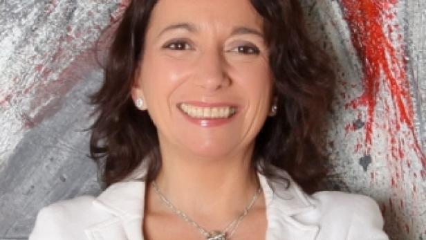 Eine lächelnde Frau in einem weißen Blazer vor einem abstrakten Hintergrund.