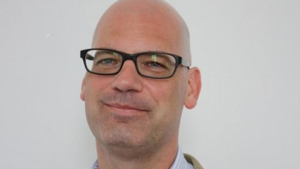 Ein Mann mit Brille und Anzug lächelt in die Kamera.