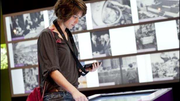 Eine Frau mit Kopfhörern interagiert mit einem interaktiven Bildschirm in einem Museum.