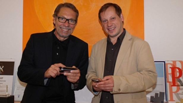 Zwei Männer stehen nebeneinander und schauen auf ihre Smartphones.