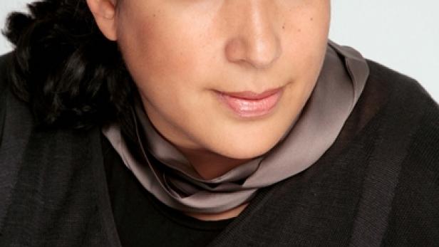 Eine Frau mit dunklen Haaren und einem grauen Schal blickt in die Kamera.