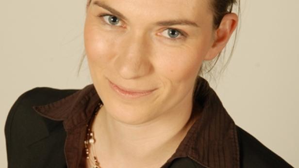 Eine Frau mit braunen Haaren und einem dunklen Blazer lächelt.