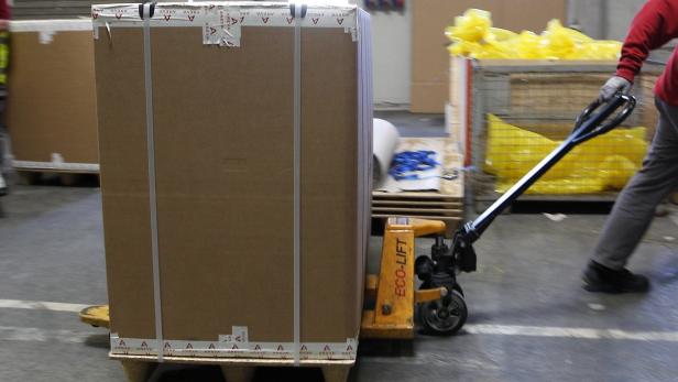 Ein Arbeiter transportiert eine große Kiste mit einem Gabelhubwagen.