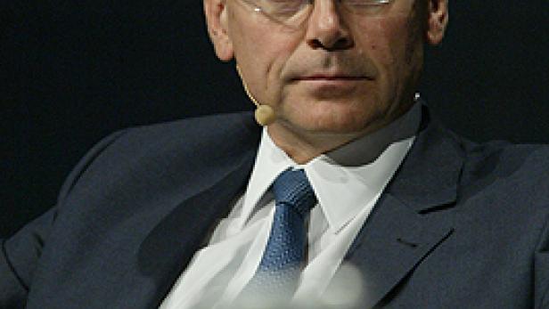 Ein Mann mit Brille und Anzug sitzt auf einem Podium.