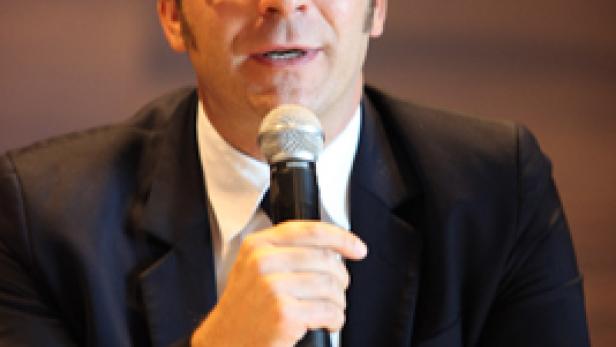Ein Mann mit Brille und Anzug spricht in ein Mikrofon.