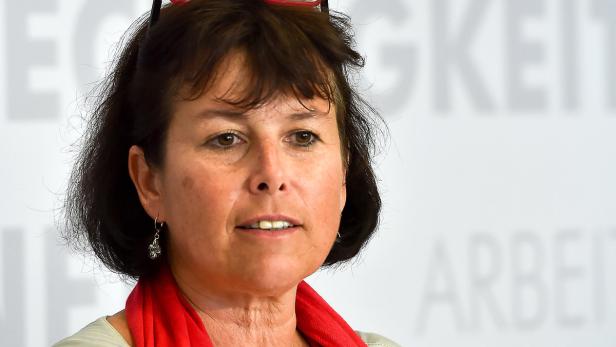 Eine Frau mit dunklen Haaren und rotem Schal vor einem hellen Hintergrund.