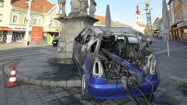 Ein ausgebranntes blaues Auto steht auf einem Platz in einer Stadt.