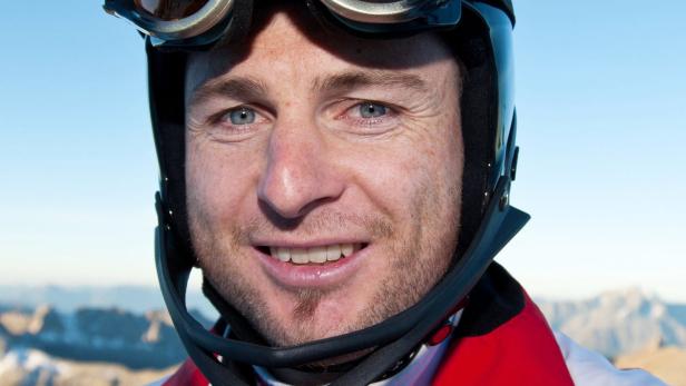 Ein Mann mit Helm und Skibrille lächelt vor einem Bergpanorama.