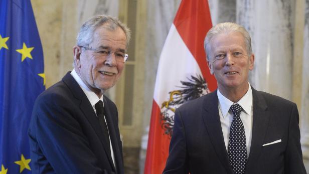 Bundespräsident Alexander Van der Bellen mit einem Mann vor der Europa- und Österreichflagge.