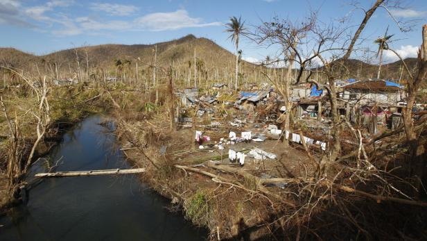 Ein zerstörtes Dorf mit beschädigten Häusern und umgestürzten Bäumen nach einem Sturm.