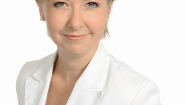 Eine Frau mit blonden Haaren und einem weißen Blazer lächelt in die Kamera.