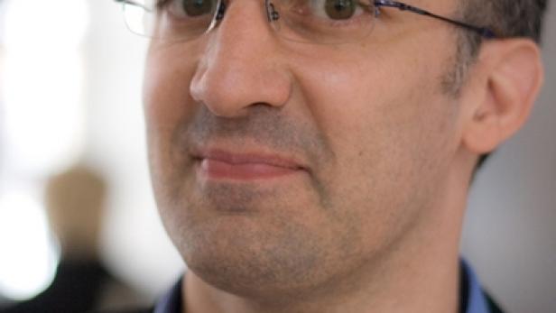 Ein Mann mit Brille und blauem Hemd blickt in die Kamera.