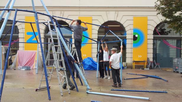 Mehrere Personen bauen eine blaue Metallkonstruktion im Freien auf.