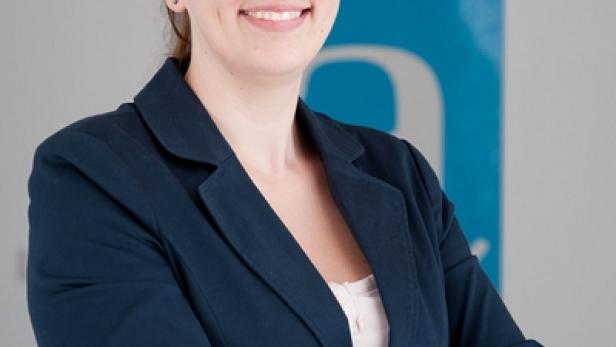 Eine Frau mit verschränkten Armen lächelt in einem blauen Blazer.