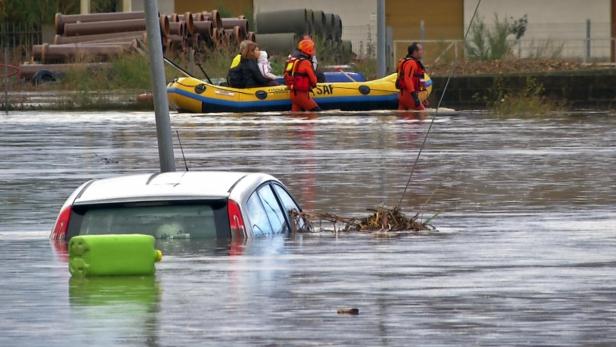 Ein überflutetes Gebiet mit einem teilweise versunkenen Auto und Rettungskräften in einem Schlauchboot.