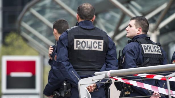 Drei Polizisten stehen hinter einem rot-weiß gestreiften Absperrband.