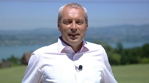Ein Mann mit weißem Hemd steht vor einer Landschaft mit See.