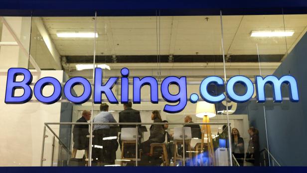 Das Logo von Booking.com hängt über einem Büro mit mehreren Personen.