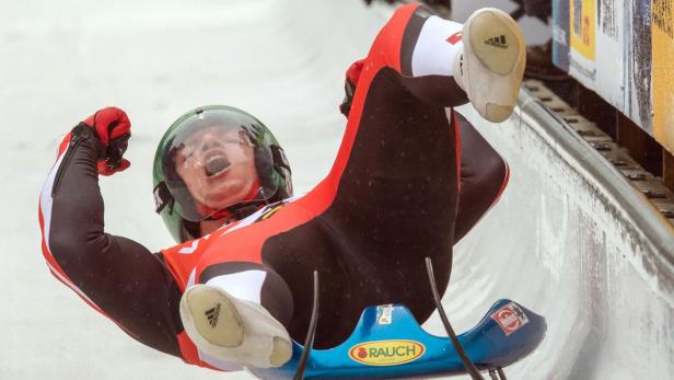 Ein Rennrodler jubelt mit erhobenen Armen auf seiner Rodel im Eiskanal.