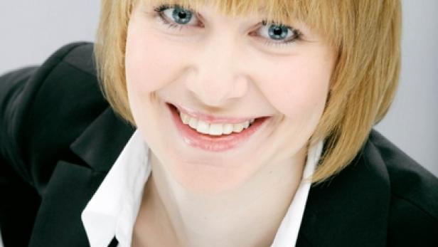 Eine lächelnde Frau mit blonden Haaren und einem schwarzen Blazer.