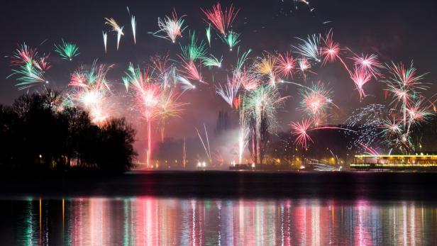 Ein farbenfrohes Feuerwerk erhellt den Nachthimmel über einem See.