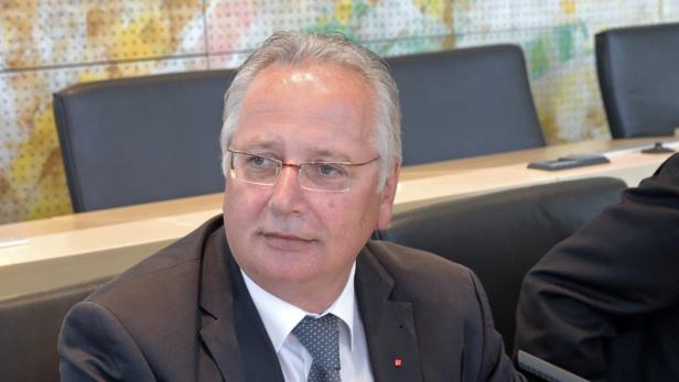 Ein Mann mit Brille und Anzug sitzt an einem Tisch.