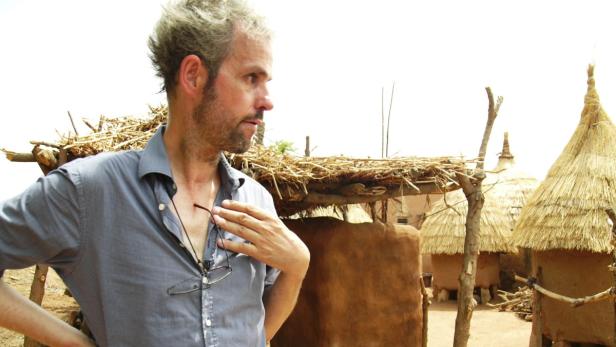 Ein Mann steht vor traditionellen afrikanischen Hütten mit Strohdächern.