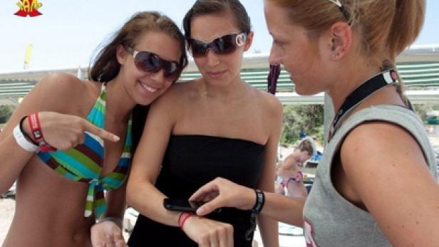Drei Frauen am Strand betrachten das Display eines Smartphones.