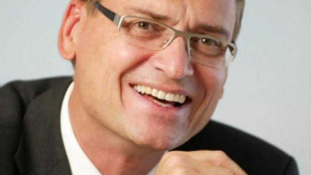 Ein lächelnder Mann mit Brille und Anzug posiert für ein Porträt.