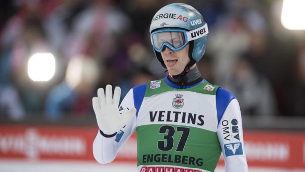 Ein Skispringer mit Helm und Brille winkt in die Kamera.