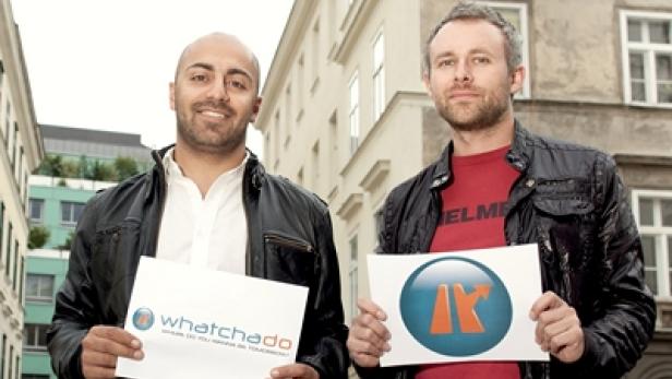 Zwei Männer posieren mit Schildern der Firma „whatchadoo“ in einer städtischen Umgebung.