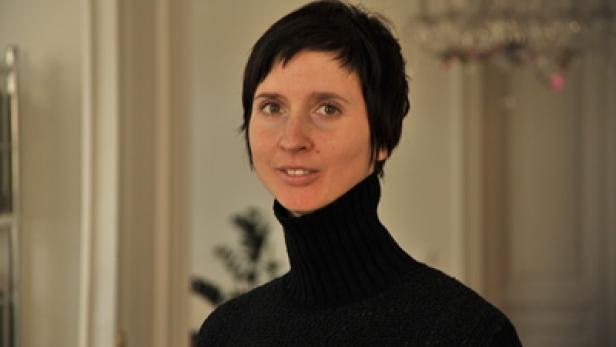 Eine Frau mit kurzen, dunklen Haaren und einem schwarzen Rollkragenpullover lächelt.
