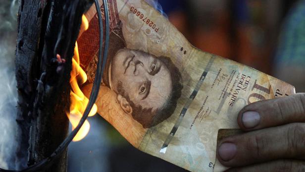 Eine Hand hält eine 100-Bolívar-Note, die in Flammen steht.