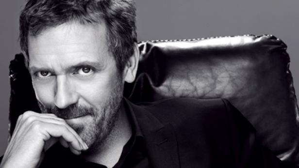 Schwarzweißporträt von Hugh Laurie, der in einem Ledersessel sitzt und nachdenklich wirkt.