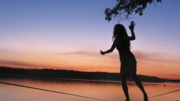 Eine Frau balanciert bei Sonnenuntergang auf einer Slackline über einem See.