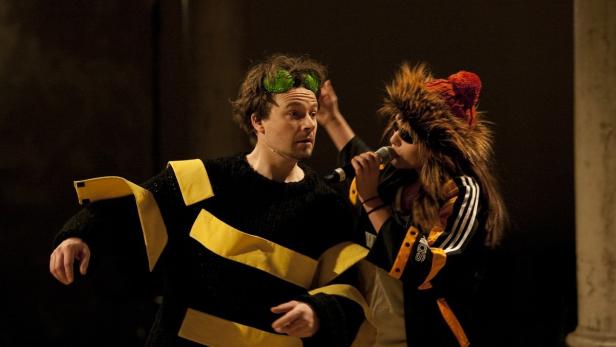 Zwei Personen in Kostümen stehen auf einer Bühne und singen.