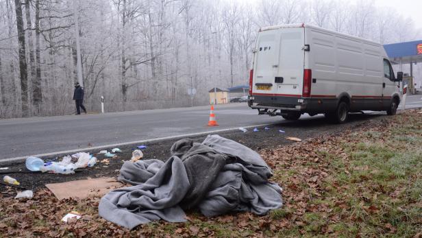 Ein weißer Lieferwagen steht am Straßenrand neben Müll und einer Decke.