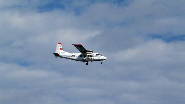 Ein kleines, weißes Flugzeug fliegt vor einem bewölkten Himmel.