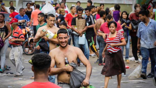 Eine Menschenmenge, einige tragen Gegenstände, geht auf einer Straße entlang.