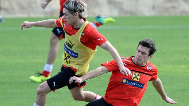 Zwei Fußballspieler kämpfen um den Ball auf einem grünen Rasen.