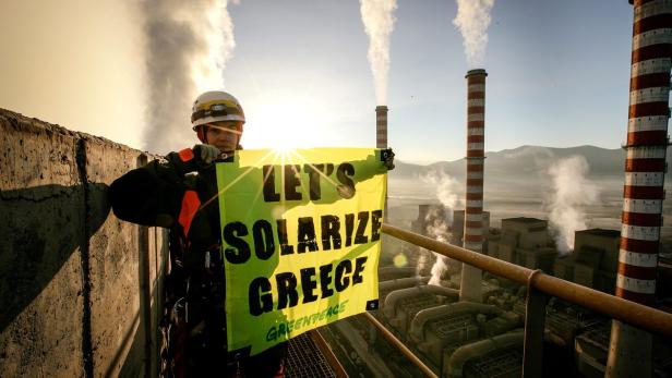 Ein Aktivist von Greenpeace hält ein Banner mit der Aufschrift „Let's Solarize Greece“ vor einem Kohlekraftwerk.