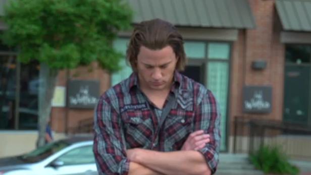 Ein Mann mit verschränkten Armen steht vor einem Gebäude.